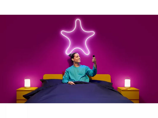 Person in bed with a neon star light above them against a purple wall.