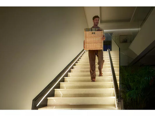 Philips Hue OmniGlow Strip Light lighting up a stairwell as a man carries a box