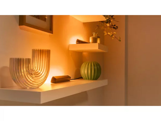 Decorative shelf with a textured vase, green fruit, and framed picture in warm indoor lighting.