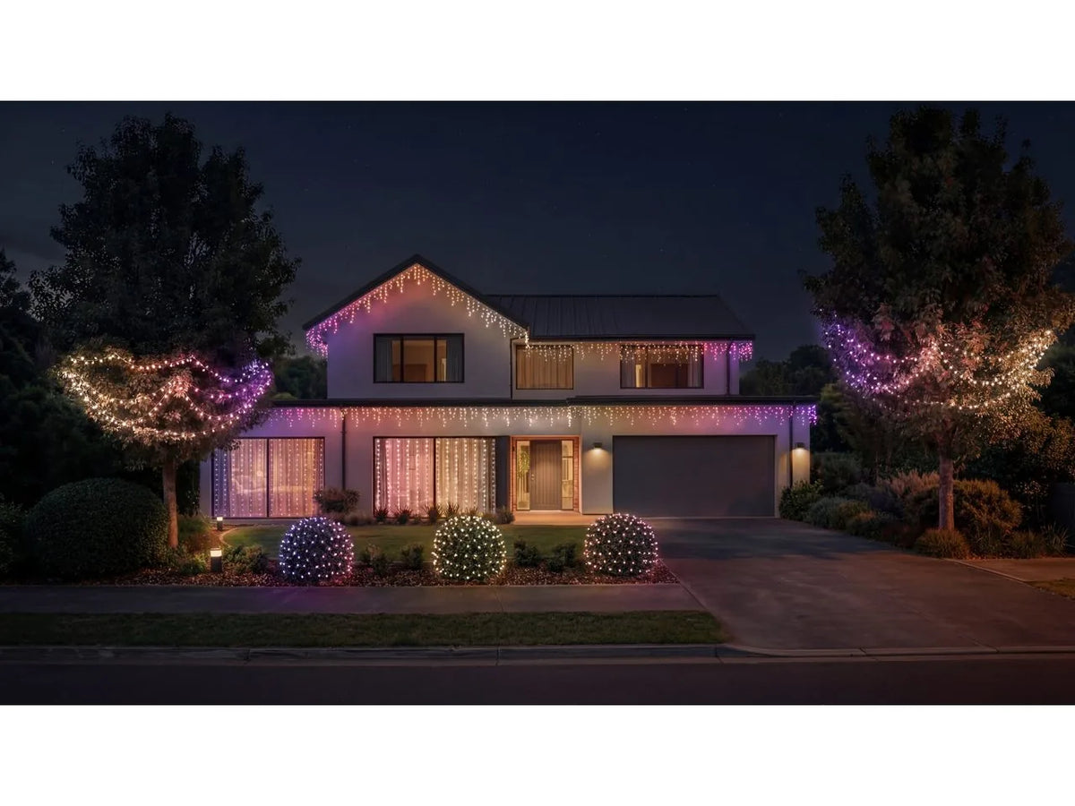 House at night decorated with Philips Hue Festavia lights, with curtain lights in the front windows, icicle lights along the roofline and globe string lights in the trees.