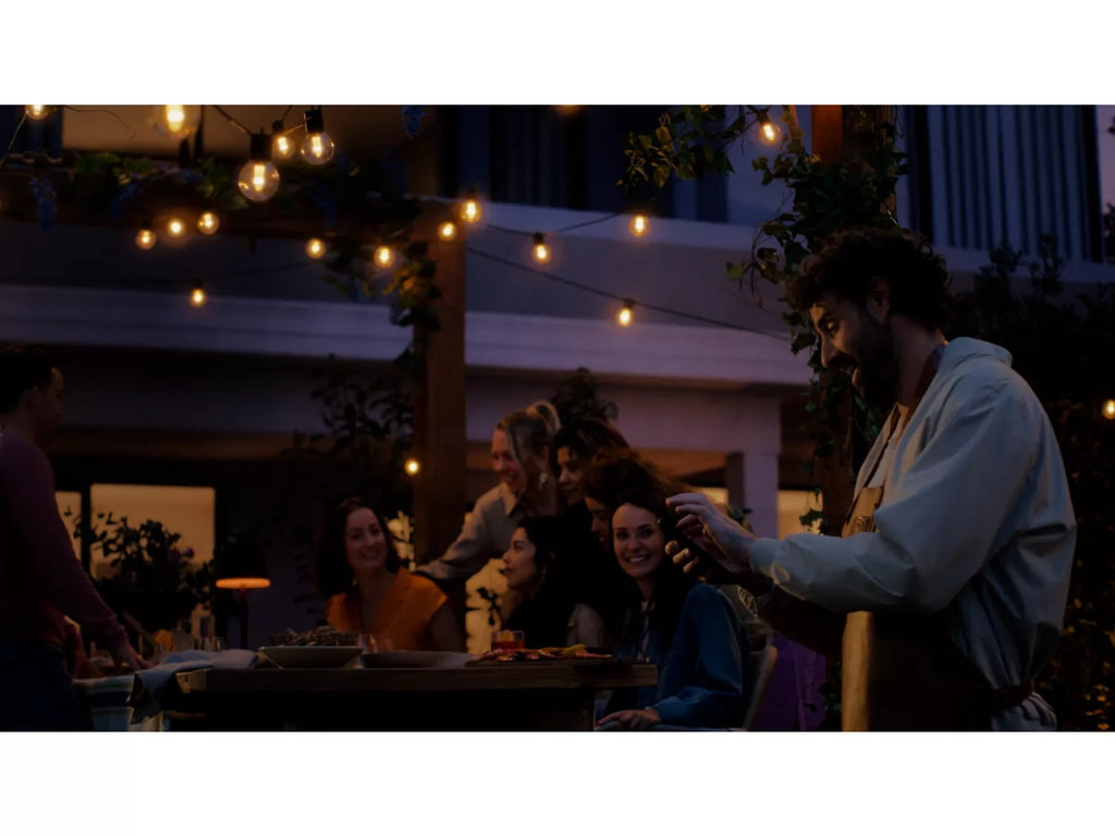 Group of people celebrating outdoors at night with hue outdoor string lights