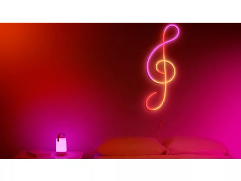 wiz Neon treble clef light on a pink wall with a small table and lamp in the foreground.