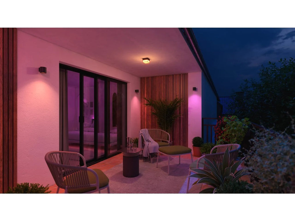 Covered patio at night with Philips Hue Muscari wall spotlights casting pink and purple light across the walls, outdoor chairs and potted plants.