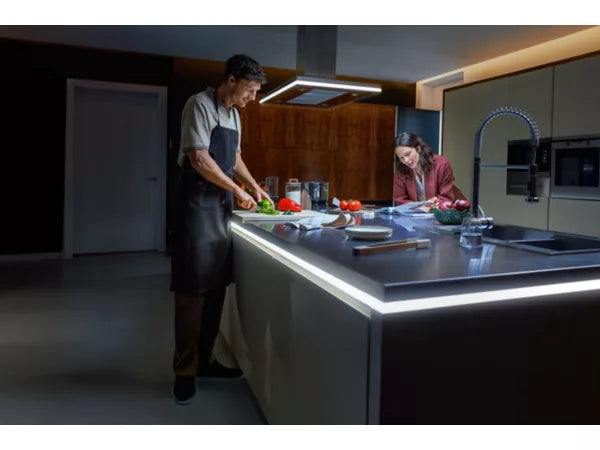 Two people in a modern kitchen preparing food lit up by the Philips Hue OmniGlow Strip Light