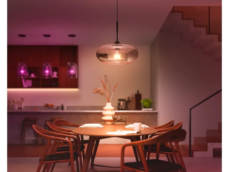 Dining area with wooden table and chairs, modern pendant light, and kitchen in the background.