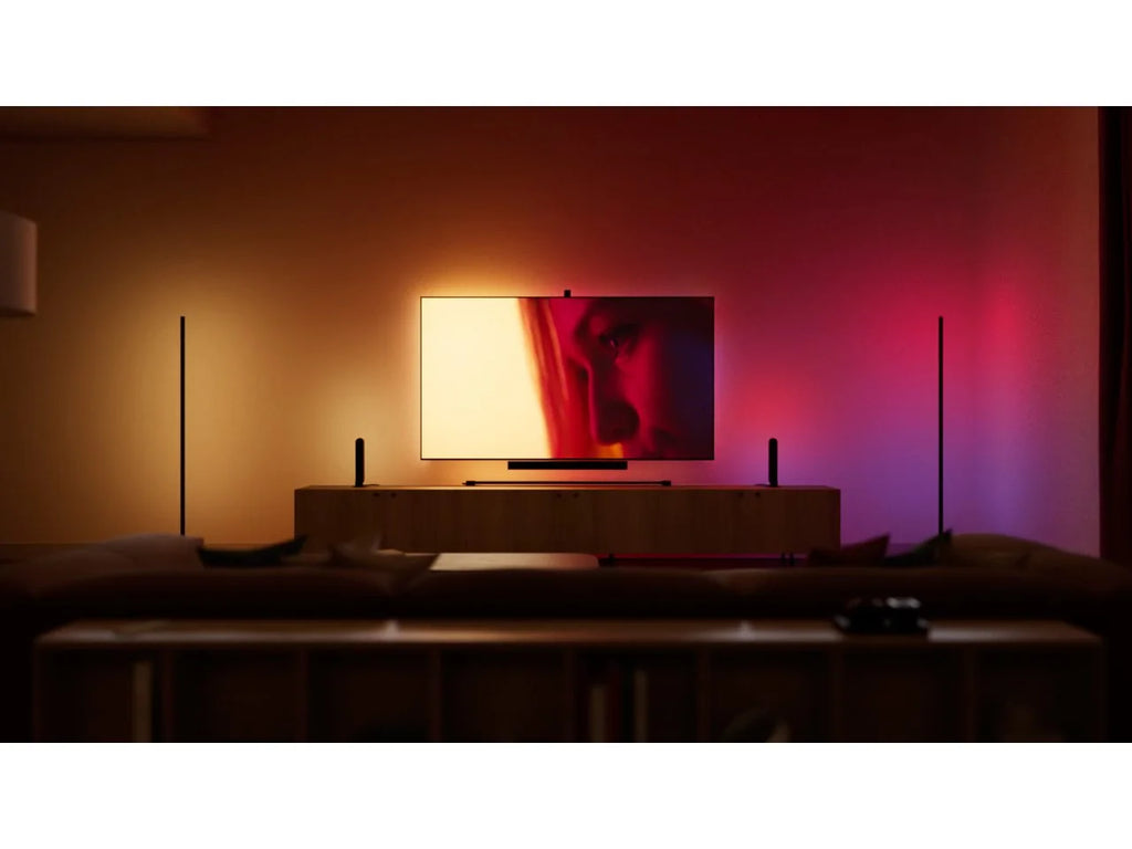 Living room at night with the Philips Hue Play Gradient Light Strip behind the TV, washing the wall in a gradient of warm amber, pink and purple light.