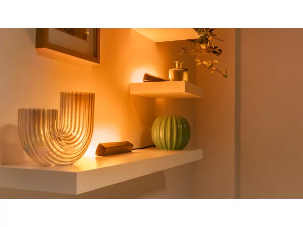 Decorative shelf with a textured vase, green fruit, and framed picture in warm indoor lighting.