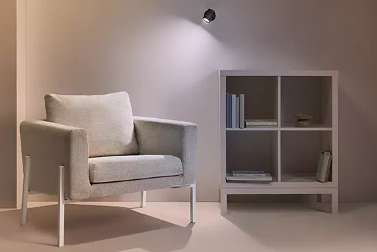Gray armchair next to a white bookshelf against a plain wall with gu10 wiz globe