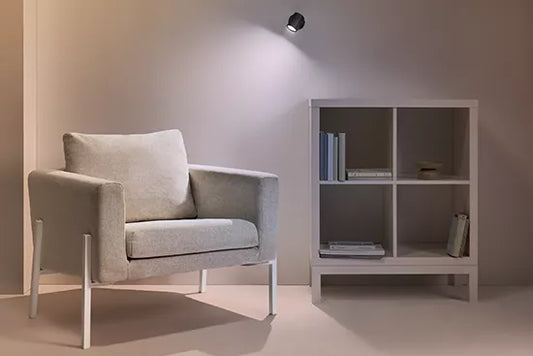 Gray armchair next to a white bookshelf against a plain wall with gu10 wiz globe