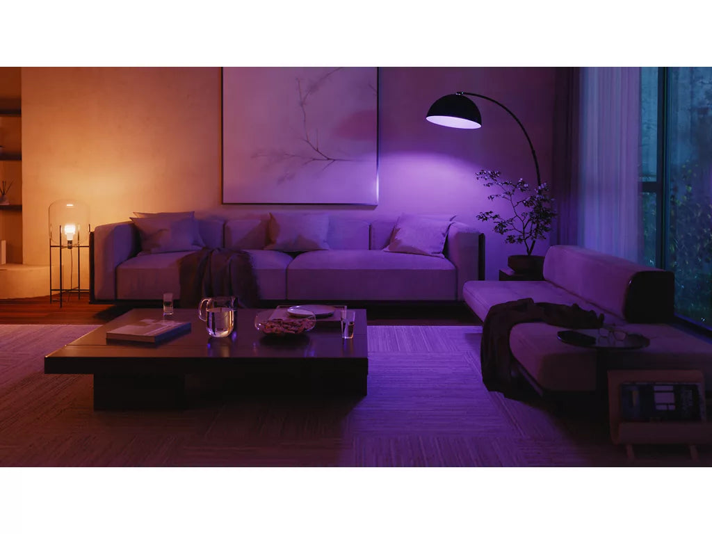 Modern living room with purple lighting, featuring a sofa, coffee table, and decorative items.
