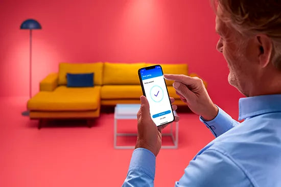 Person using a smartphone app in a modern living room with a yellow sofa and red walls.